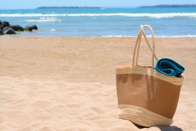 Photo of Soft blue towel in beach bag on sand near sea, space for text