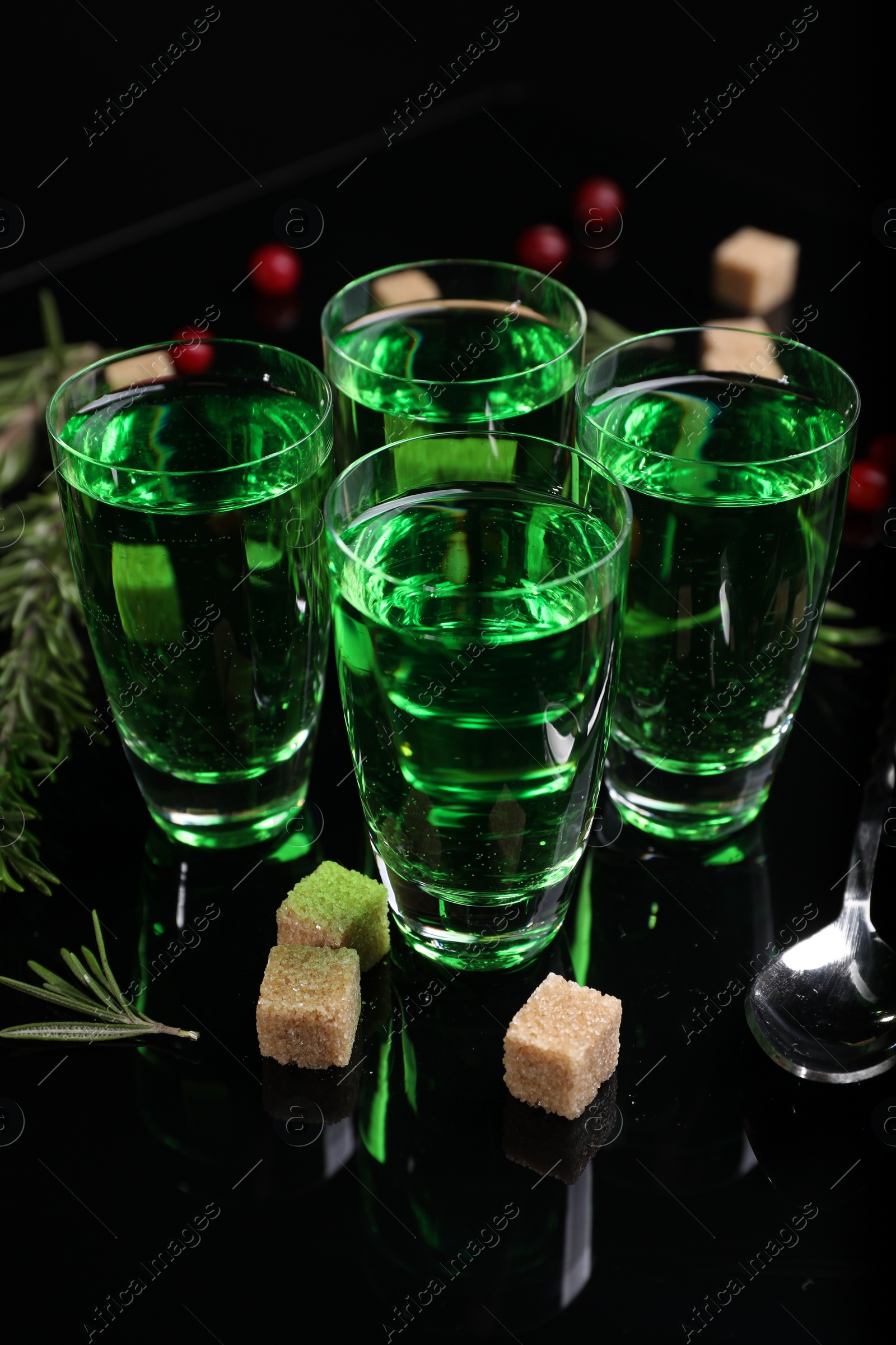 Photo of Absinthe in shot glasses, rosemary, brown sugar and spoon on mirror table. Alcoholic drink