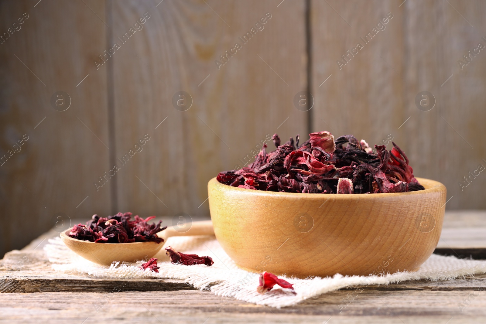 Photo of Dry hibiscus tea in bowl on wooden table, space for text