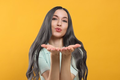 Portrait of beautiful woman with ash hair color blowing kiss on orange background