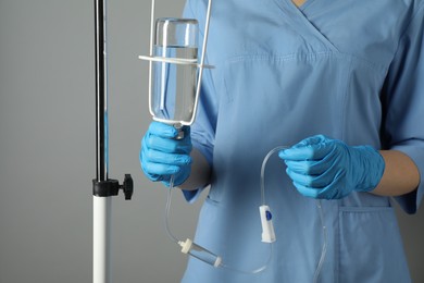 Nurse with IV infusion set on grey background, closeup