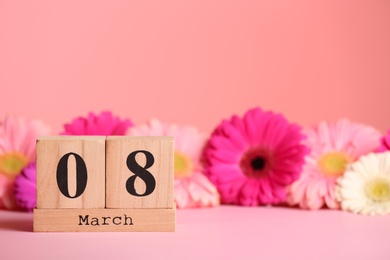 Photo of Wooden block calendar and flowers on table against color background, space for text. International Women's Day
