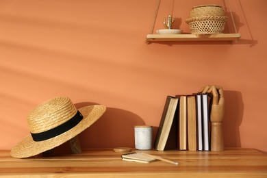 Photo of Books and straw hat on wooden table near brown wall. Interior design