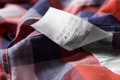 Photo of Clothing label on beautiful checkered garment, closeup