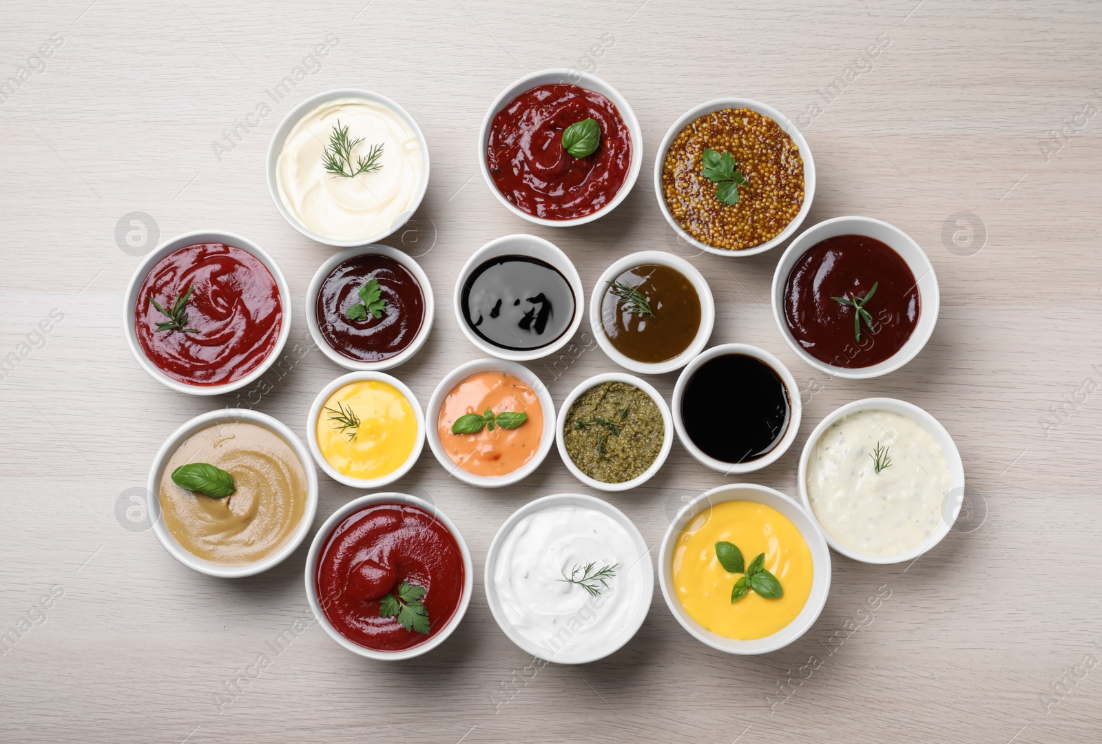 Photo of Many bowls with different sauces and herbs on wooden table