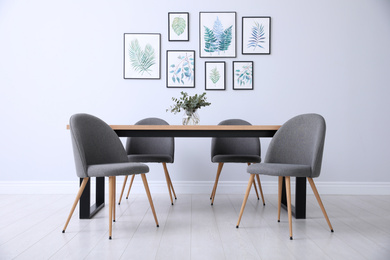Photo of Stylish room interior with modern table, chairs and paintings of tropical leaves. Idea for design