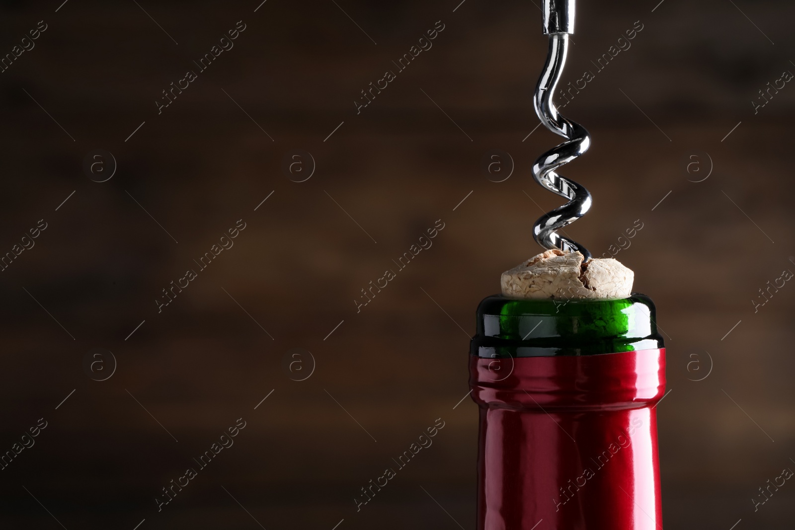 Photo of Opening wine bottle with corkscrew on dark brown background, closeup. Space for text