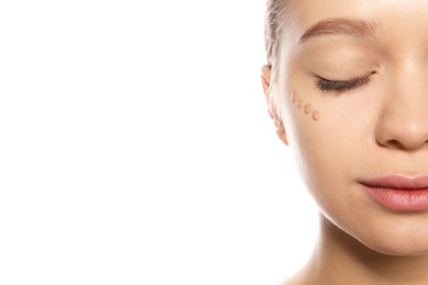 Young woman with liquid foundation on her face against white background, closeup