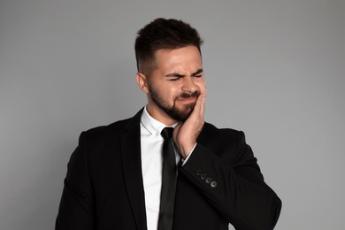 Businessman suffering from toothache on light grey background