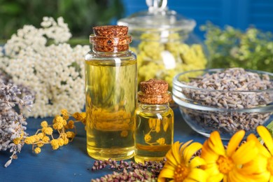 Photo of Bottles of essential oils and different herbs on blue wooden table, closeup