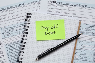 Image of Reminder note with phrase Pay Off Debt, notebook and pen on documents, flat lay