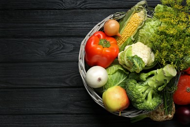 Photo of Different fresh vegetables in wicker basket on black wooden table, top view with space for text. Farmer harvesting