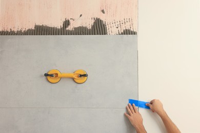 Worker installing ceramic tile on wall indoors, closeup