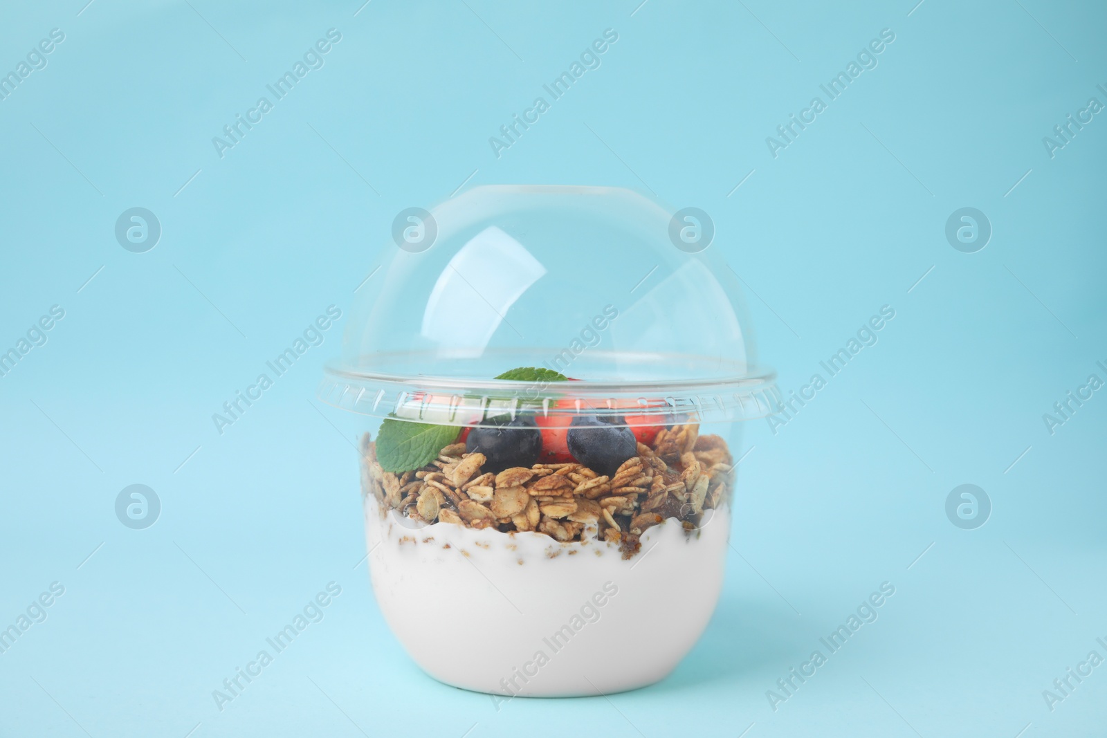 Photo of Tasty granola with berries and yogurt in plastic cup on light blue background