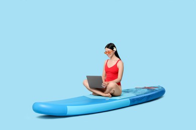 Photo of Happy woman with laptop on SUP board against light blue background