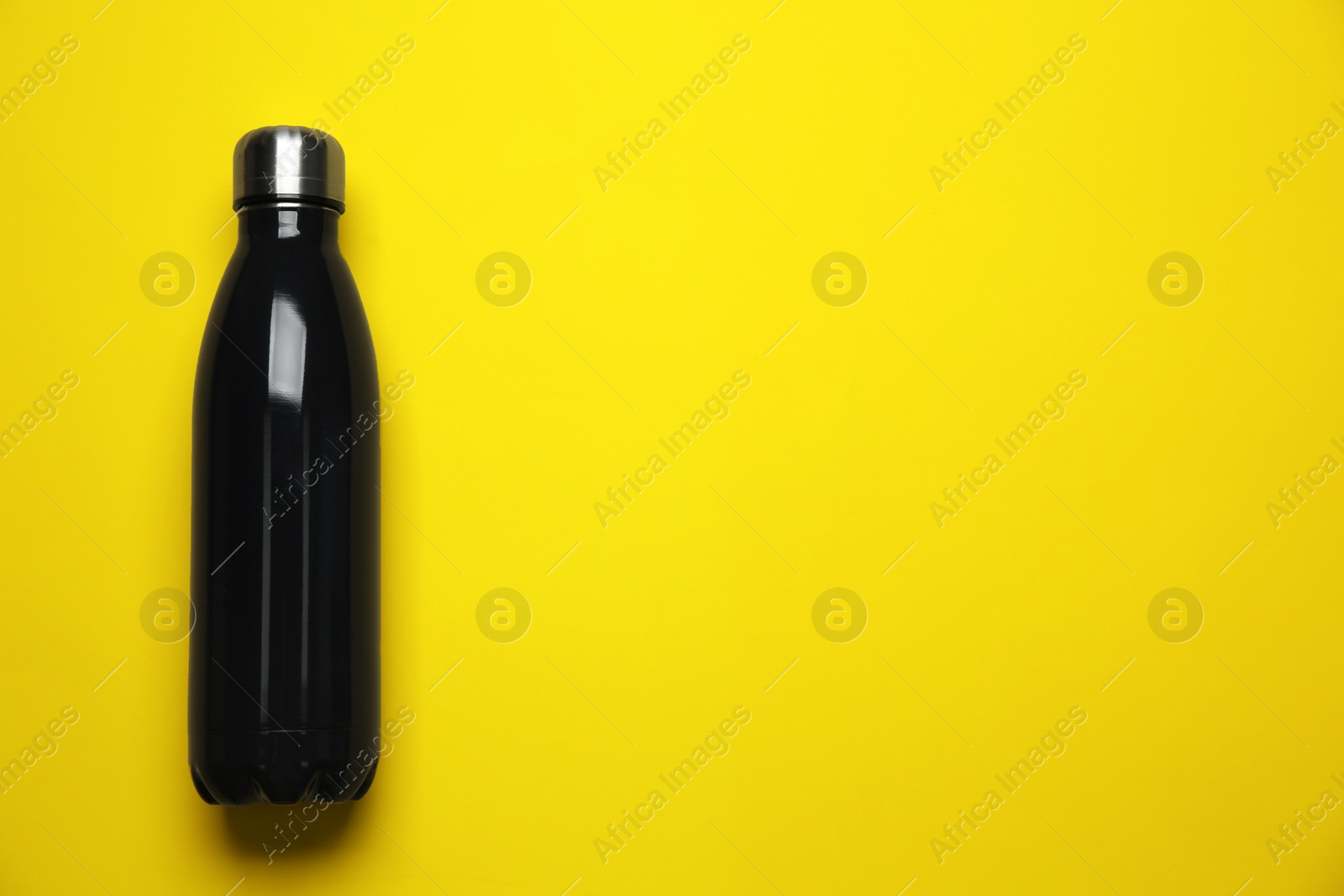 Photo of Black thermo bottle on yellow background, top view. Space for text