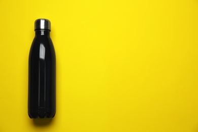 Black thermo bottle on yellow background, top view. Space for text