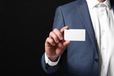 Businessman holding blank business card on black background, closeup. Space for text