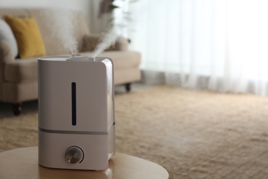 Photo of Modern air humidifier on wooden table indoors. Space for text