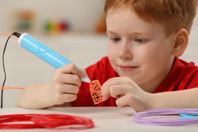 Boy drawing with stylish 3D pen at white table, selective focus