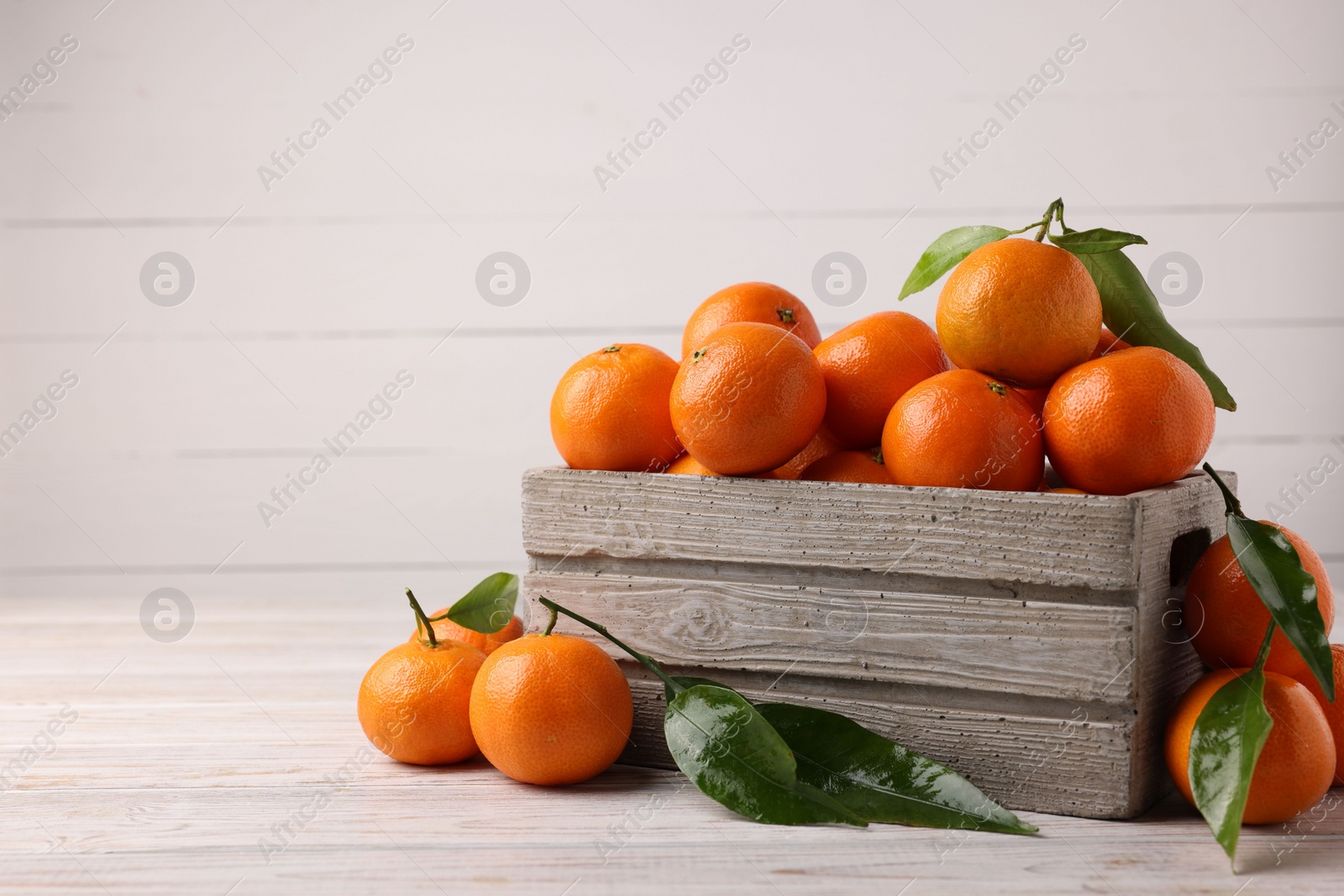 Photo of Delicious tangerines with leaves on light wooden table. Space for text