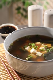 Photo of Bowl of delicious miso soup with tofu and chopsticks on table, closeup