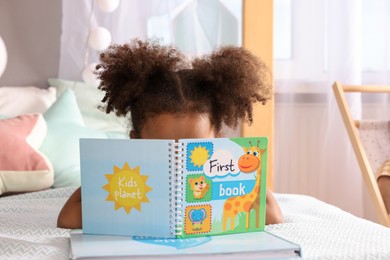 African American girl reading book on bed at home