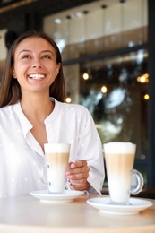 Photo of Beautiful young woman with coffee at table in cafe
