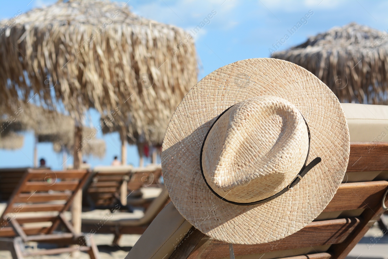Photo of Stylish straw hat on wooden sunbed at beach, space for text