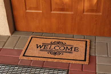 Photo of Door mat with word Welcome on street tiles near entrance