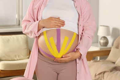 Pregnant woman with kinesio tapes on her belly at home, closeup