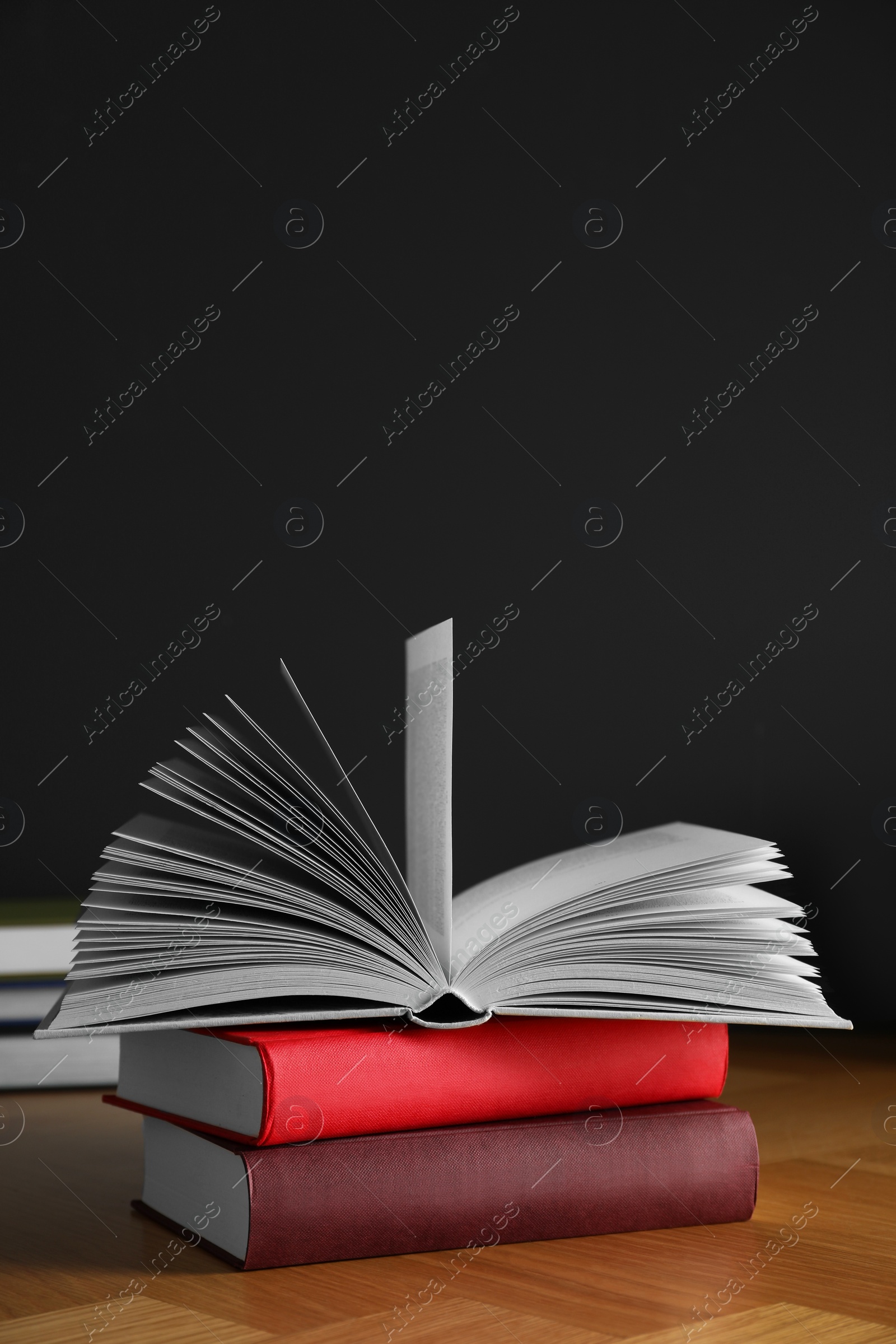 Photo of Many books stacked on wooden table near black wall