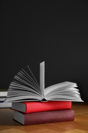 Many books stacked on wooden table near black wall