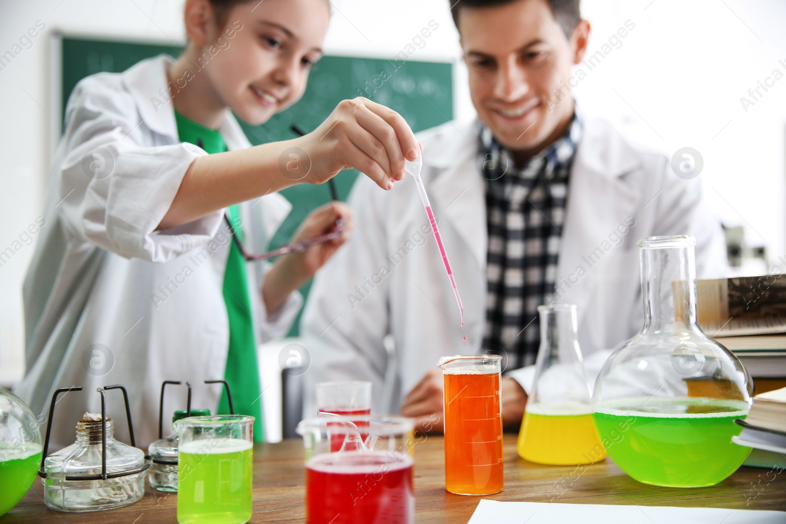 Photo of Teacher with pupil making experiment at table in chemistry class, focus on hand