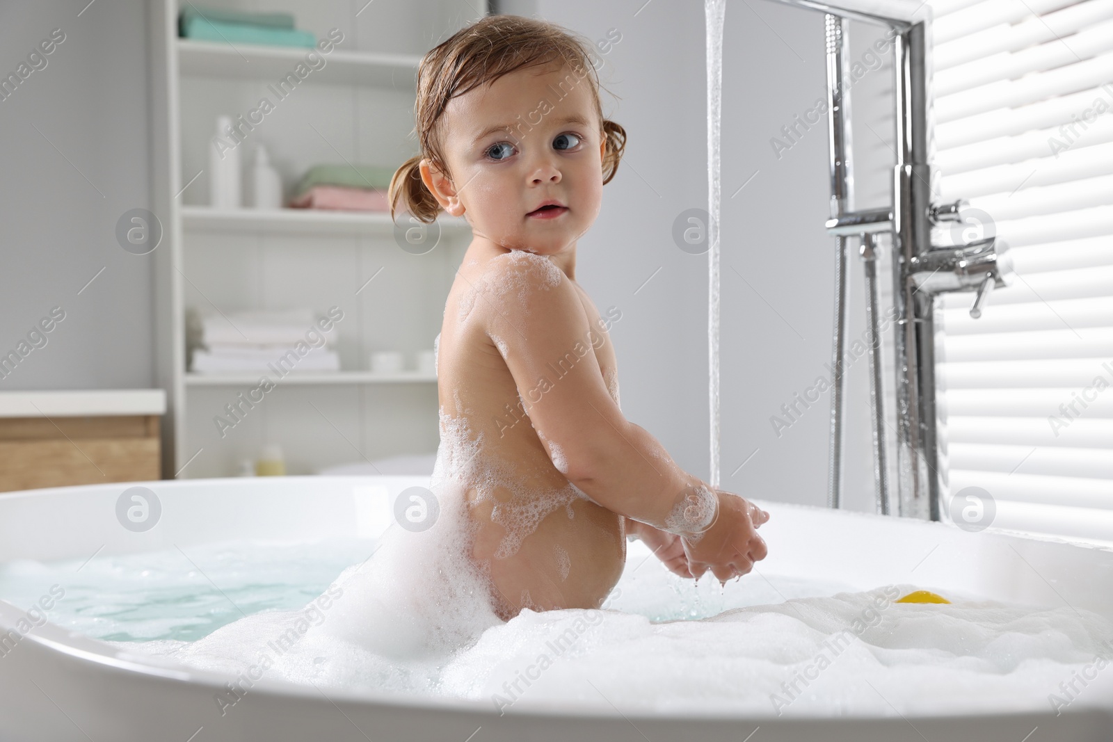 Photo of Cute little girl taking foamy bath at home