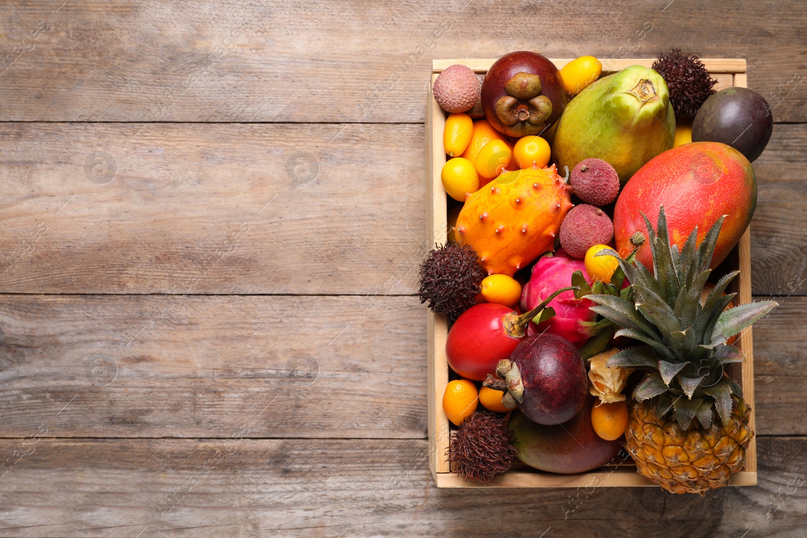 Photo of Crate with different exotic fruits on wooden table, top view. Space for text