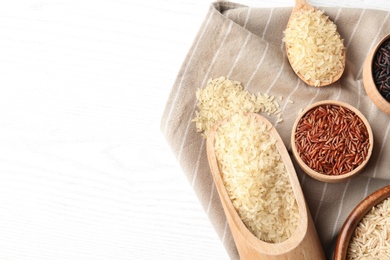 Photo of Flat lay composition with brown and other types of rice on white wooden background. Space for text