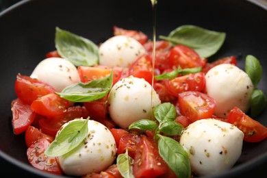 Photo of Pouring oil onto tasty salad Caprese with tomatoes, mozzarella balls and basil, closeup