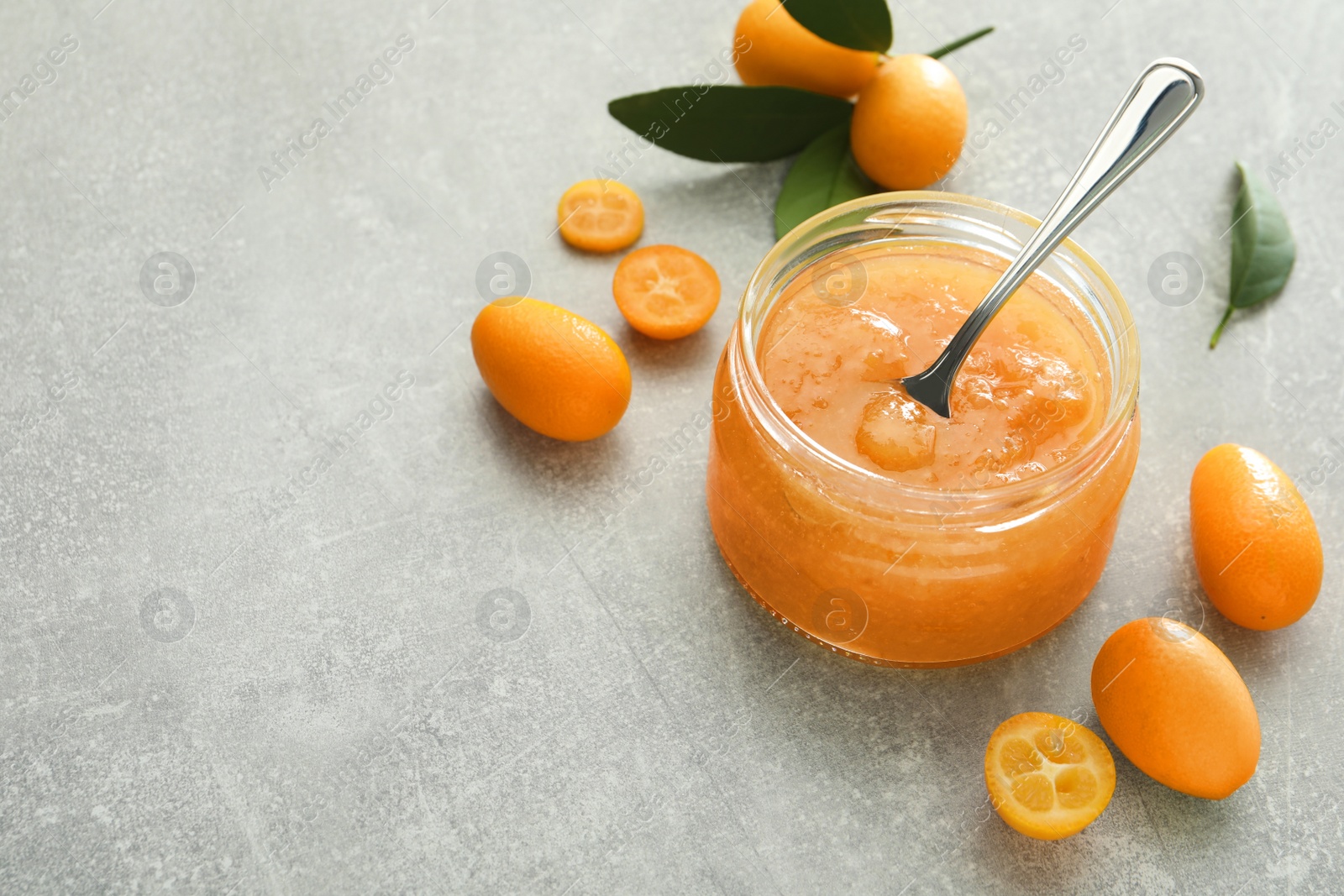 Photo of Delicious kumquat jam and fresh fruits on light grey table. Space for text