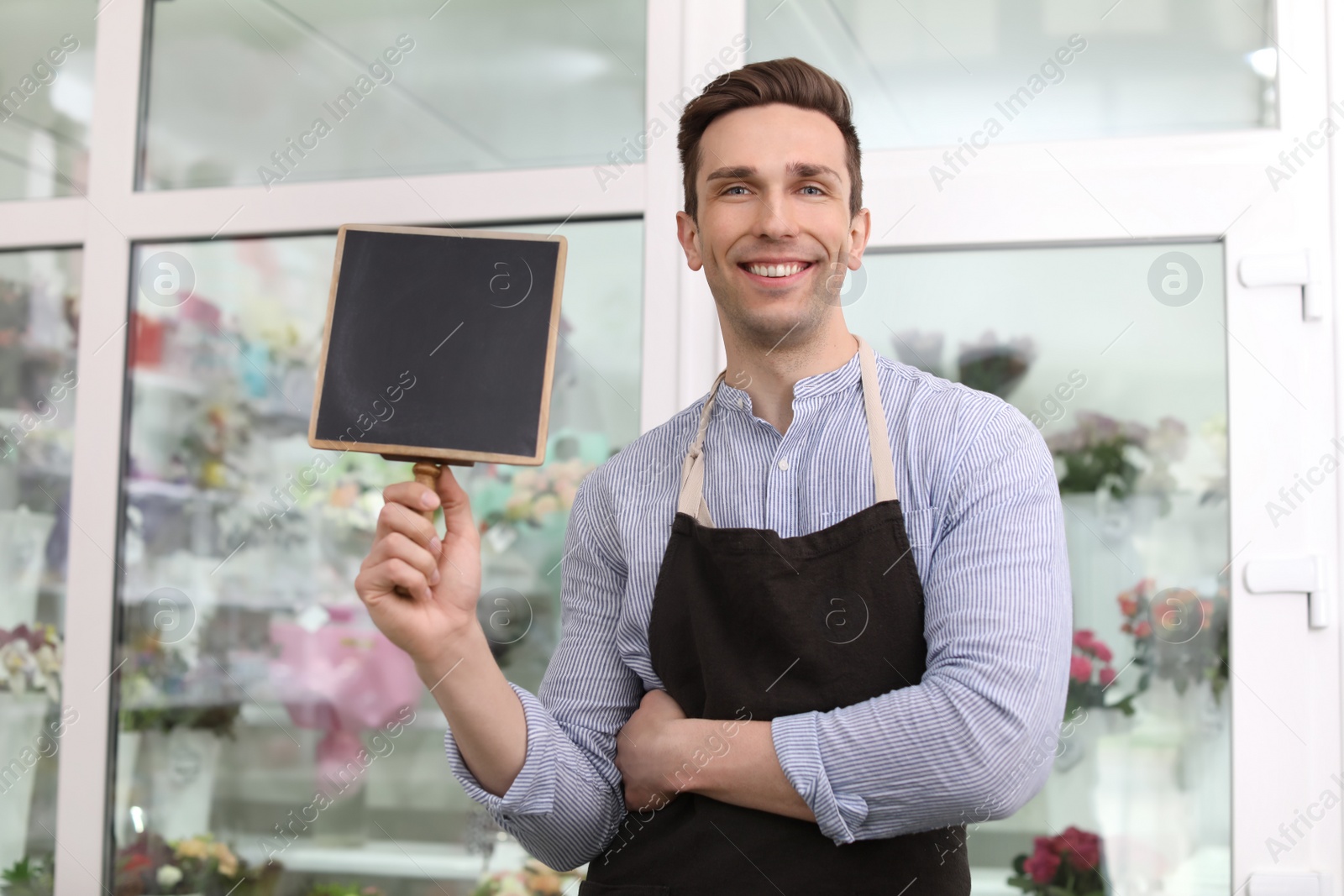 Photo of Male florist holding small chalkboard at workplace