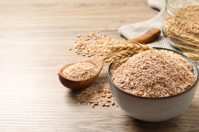 Photo of Wheat bran and spikelets on wooden table. Space for text