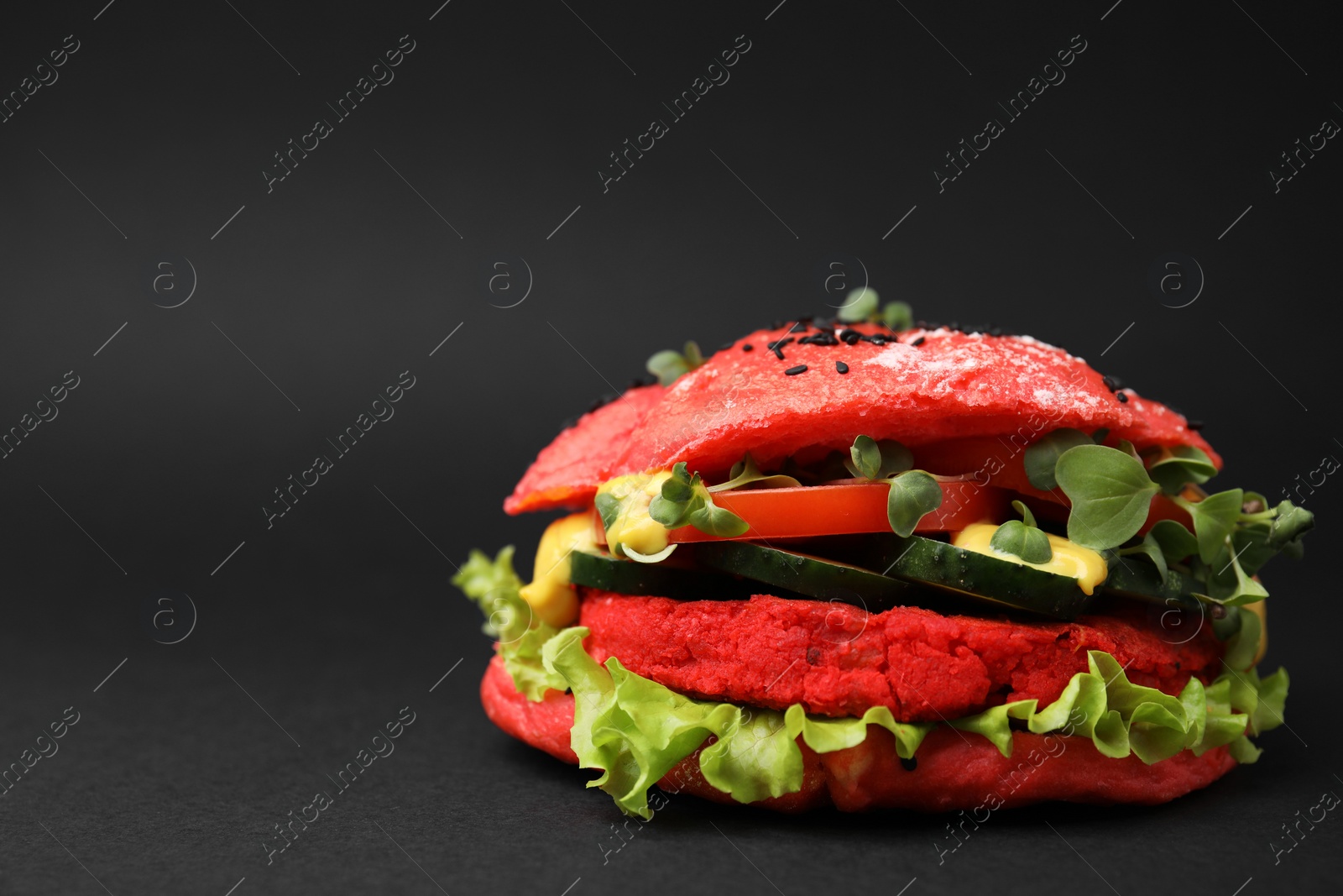 Photo of Tasty pink vegan burger with vegetables, patty and microgreens on black background, closeup. Space for text