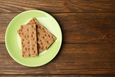Photo of Plate with rye crispbreads on wooden table, top view. Space for text