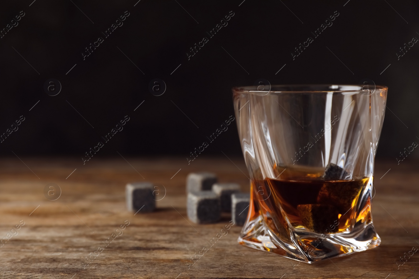 Photo of Golden whiskey in glass with cooling stones on table. Space for text