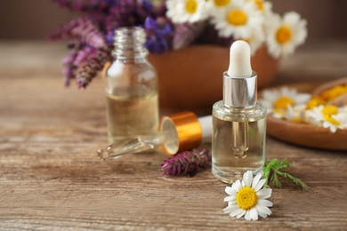 Photo of Bottles of essential oils and wildflowers on wooden table, space for text