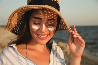 Happy young woman with sun protection cream on face at beach