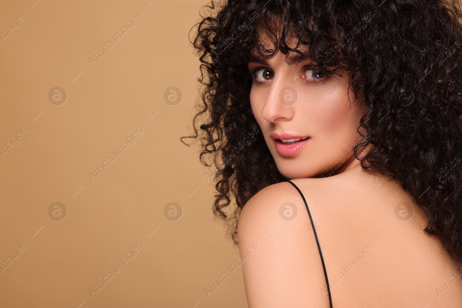 Photo of Beautiful young woman with long curly hair on beige background. Space for text