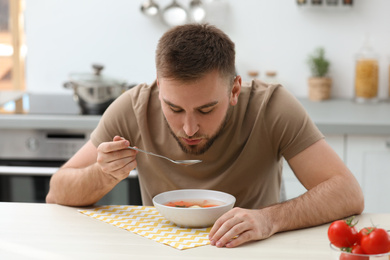 Photo of Young man eating tasty vegetable soup at table in kitchen