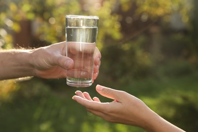 Photo of Man giving glass of fresh water to woman outdoors, closeup