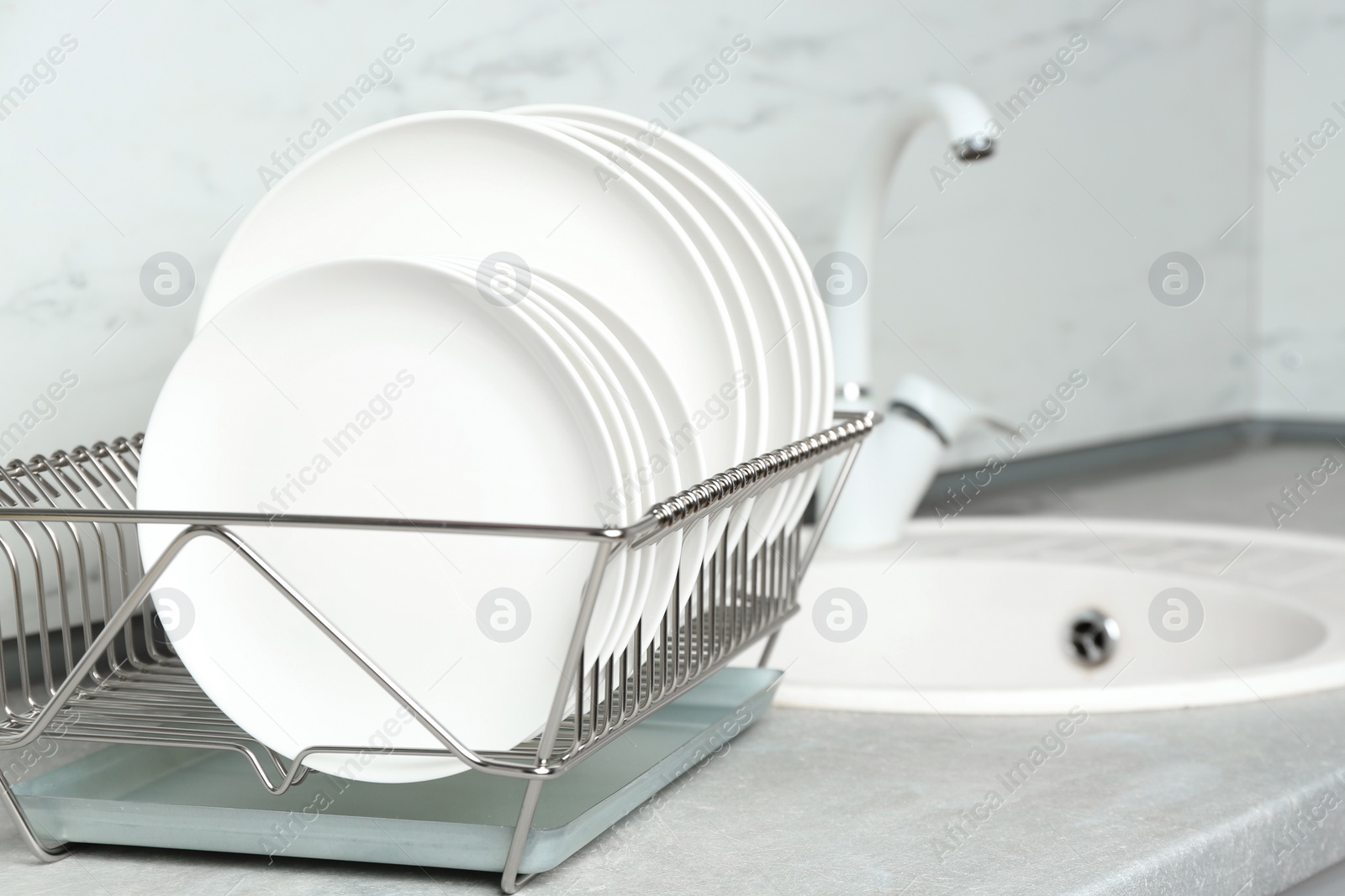 Photo of Different clean plates in dish drying rack on kitchen counter